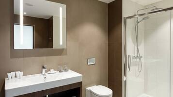 A modern bathroom with a large mirror, a white sink with toiletries, and a glass-enclosed shower.