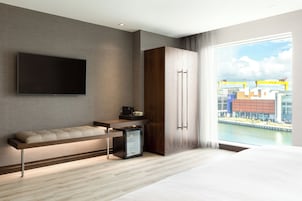 Habitación de hotel moderna con televisión de pantalla plana, sofá, refrigerador pequeño y ventana grande con vistas a la ciudad.