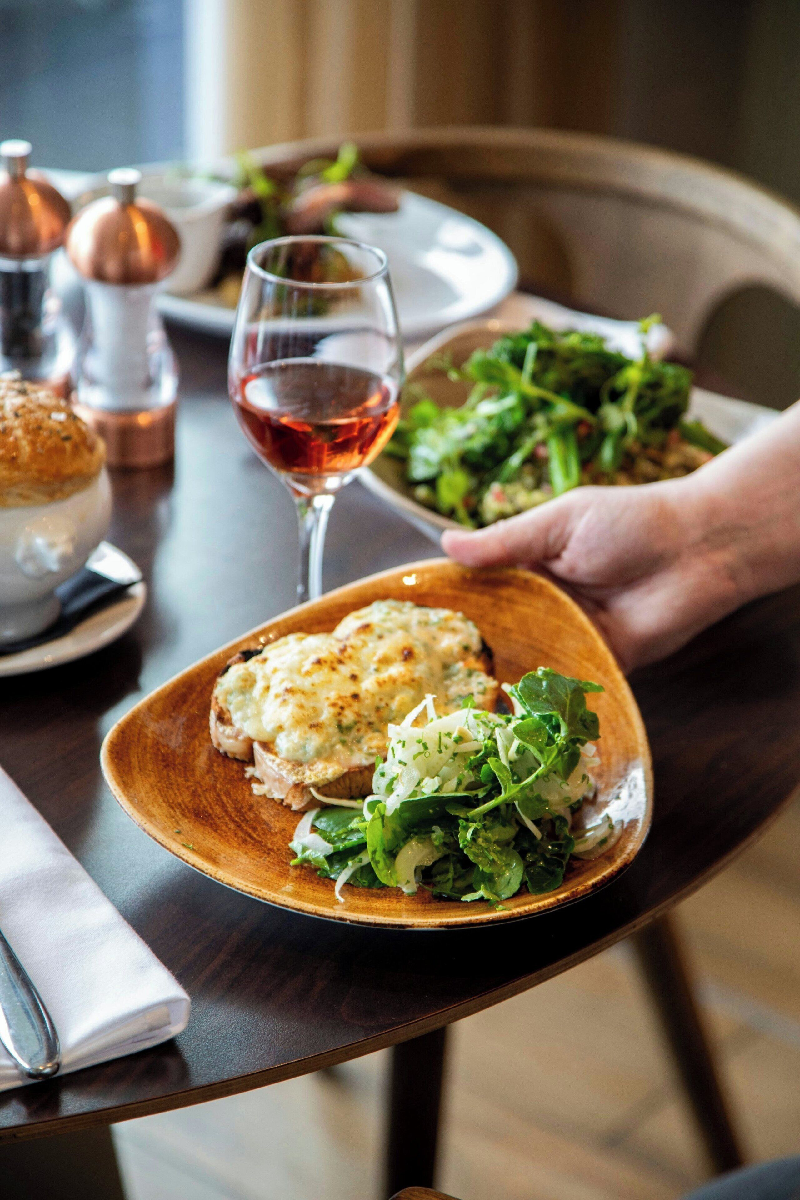 Une table en bois avec une assiette de nourriture, un verre de vin rouge et un saladier.