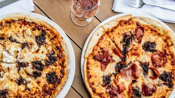 A wooden table with four pizzas, each with different toppings, and a glass of red wine.