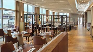 A modern restaurant with high ceilings, large windows, and a variety of seating options including round tables and sofas.