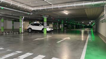 Un garaje de estacionamiento con pilares verdes, flechas direccionales blancas y un coche blanco estacionado.