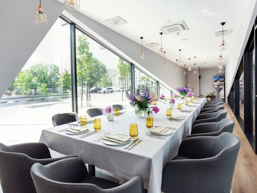 Ein Restaurant mit einem langen Esstisch, großen Fenstern und moderner Pendelleuchten.