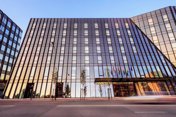Un hotel moderno con fachada de vidrio, una entrada destacada y banderas en el exterior.