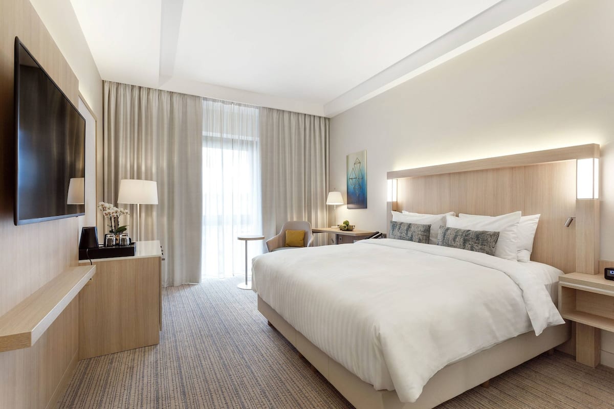 Een hotelkamer met een groot bed, een bureau, een stoel, een televisie en een raam met gordijnen.