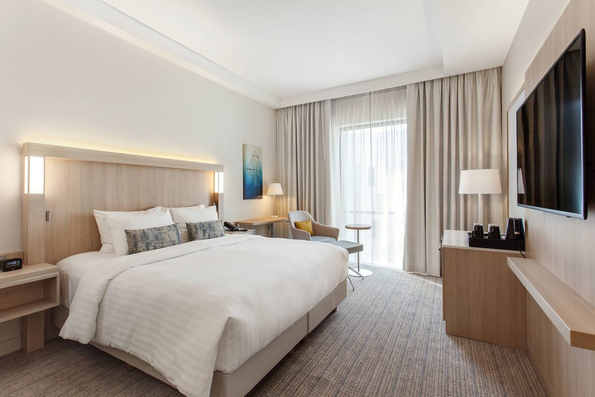 Een hotelkamer met een groot bed, nachtkastjes, een bureau, een stoel, een televisie en een raam met gordijnen.