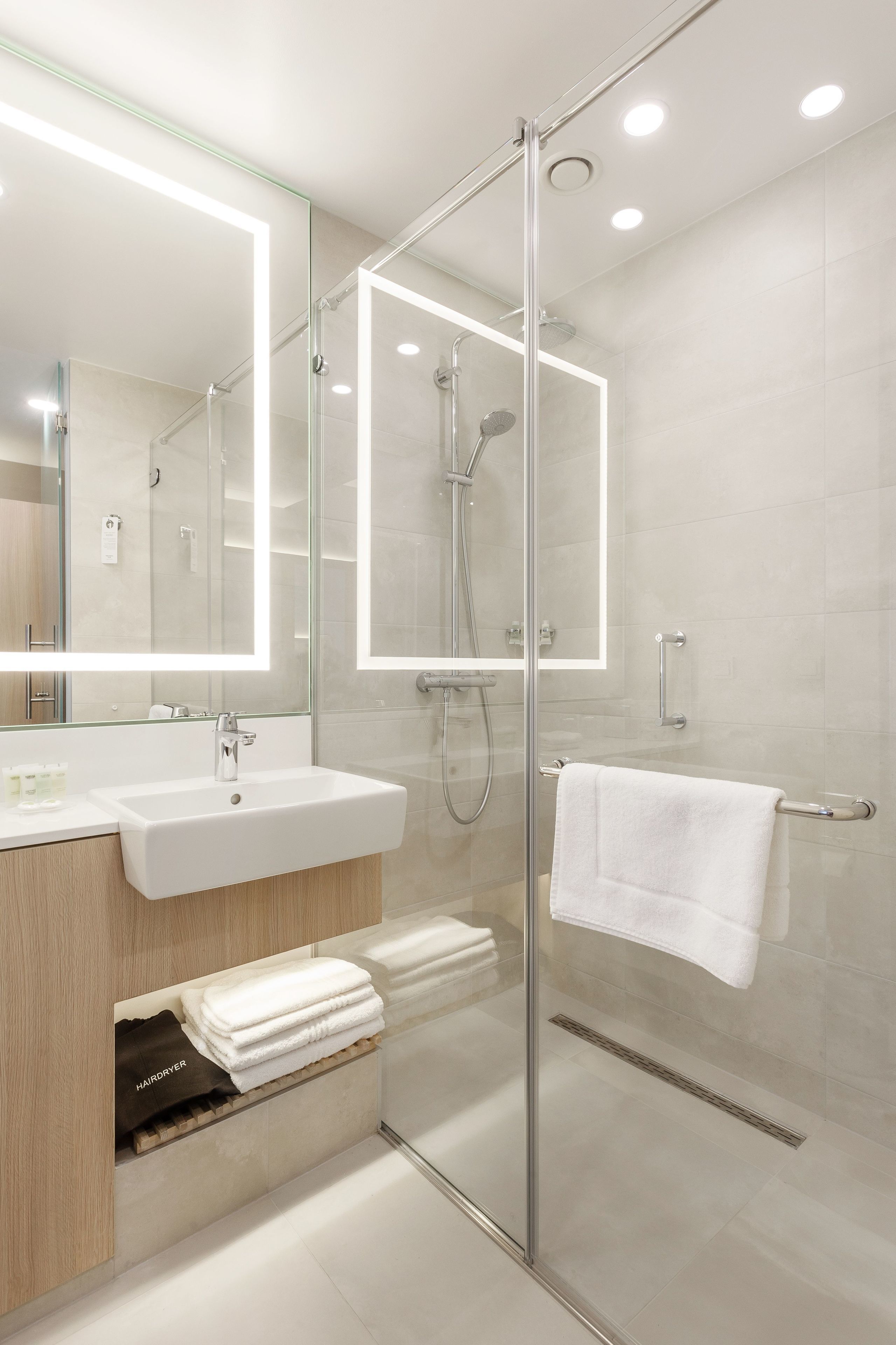 Un baño moderno con ducha de vidrio, tocador con lavamanos y espejo con iluminación integrada.