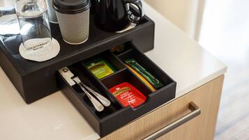 Un minibar de hotel con una cafetera, bolsitas de té y un recipiente de vidrio.