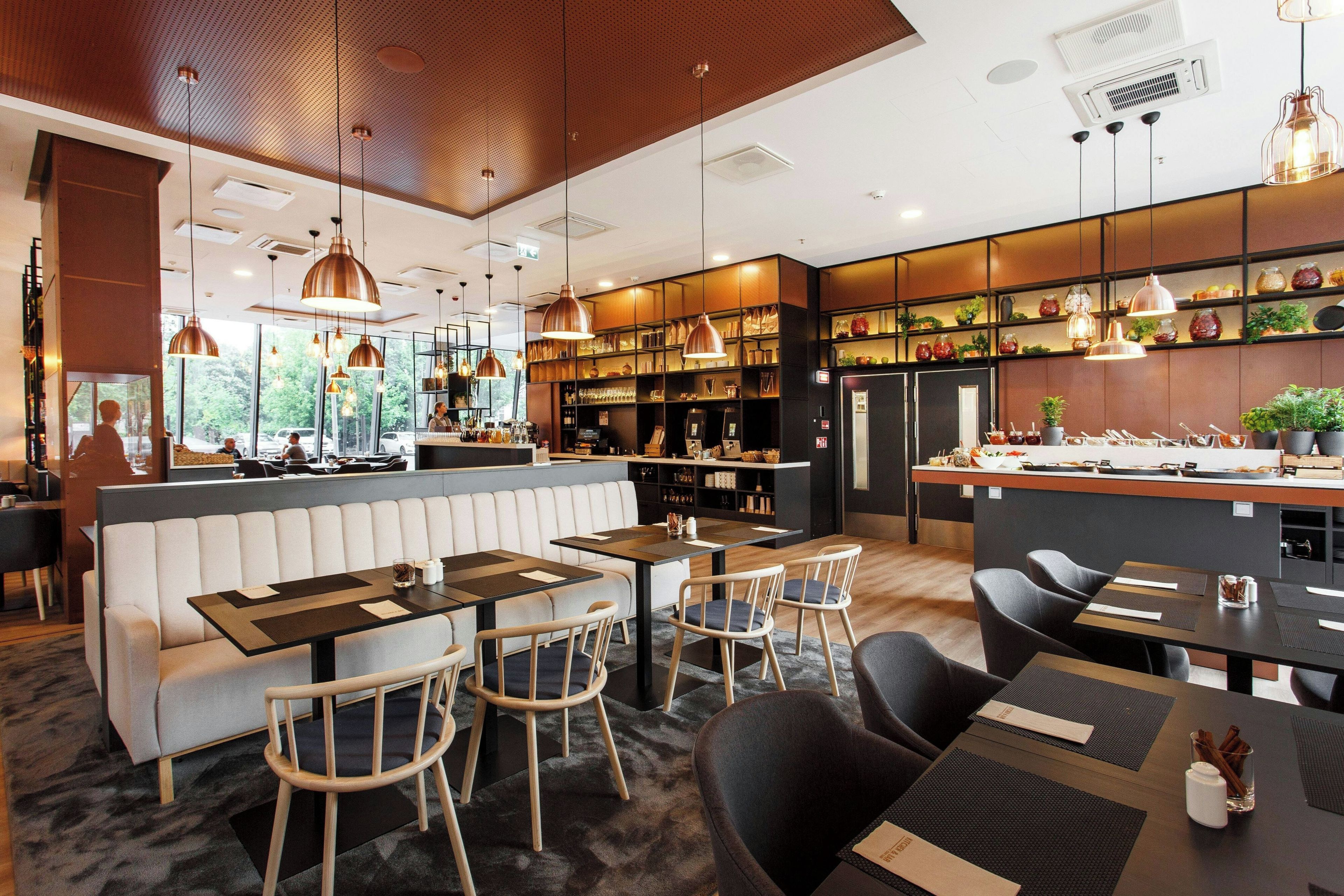 Un intérieur de restaurant moderne, avec un bar, des espaces aménagés pour s’asseoir et une vue sur l’extérieur.