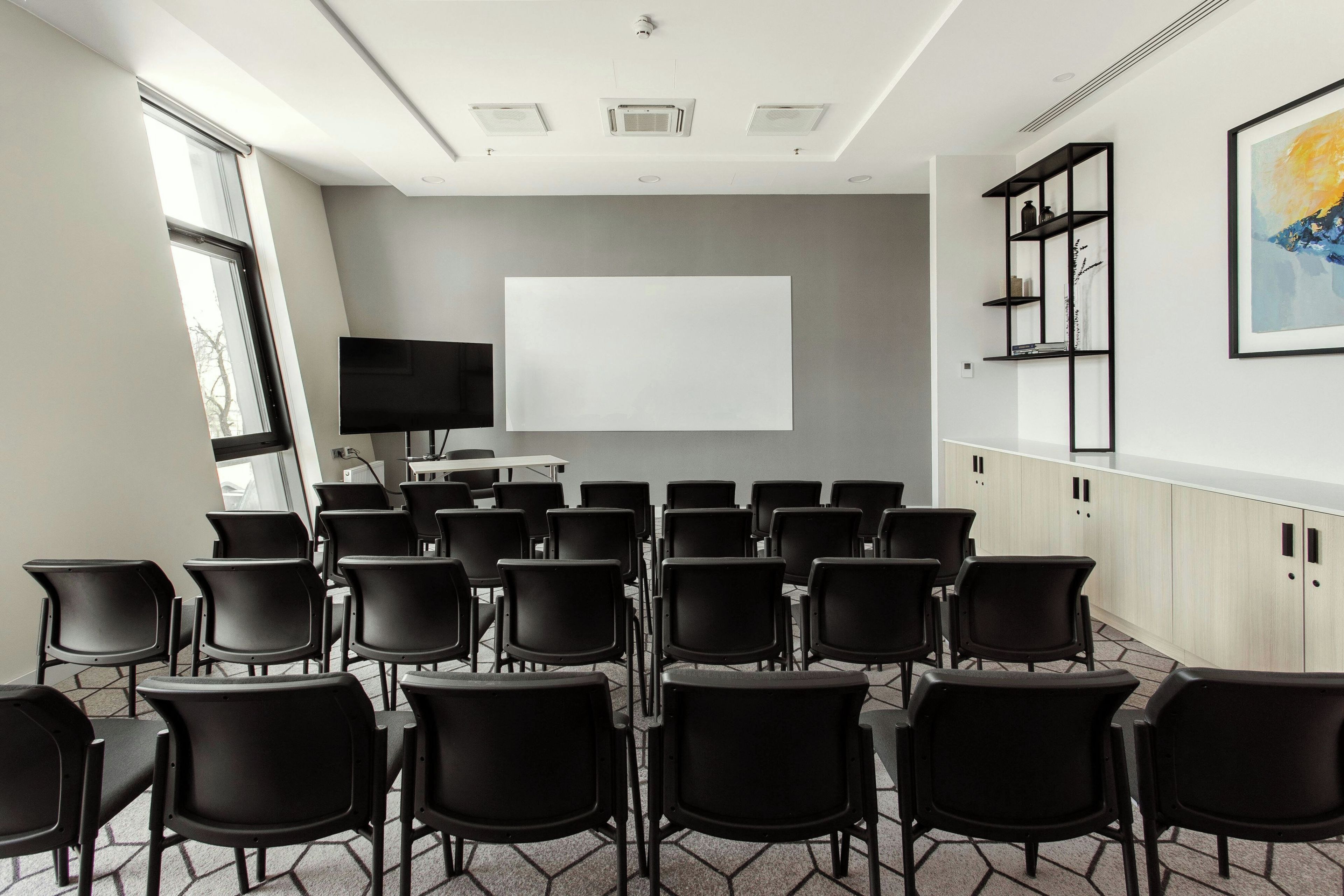 A conference room with a whiteboard, projector, and black chairs arranged for a meeting.