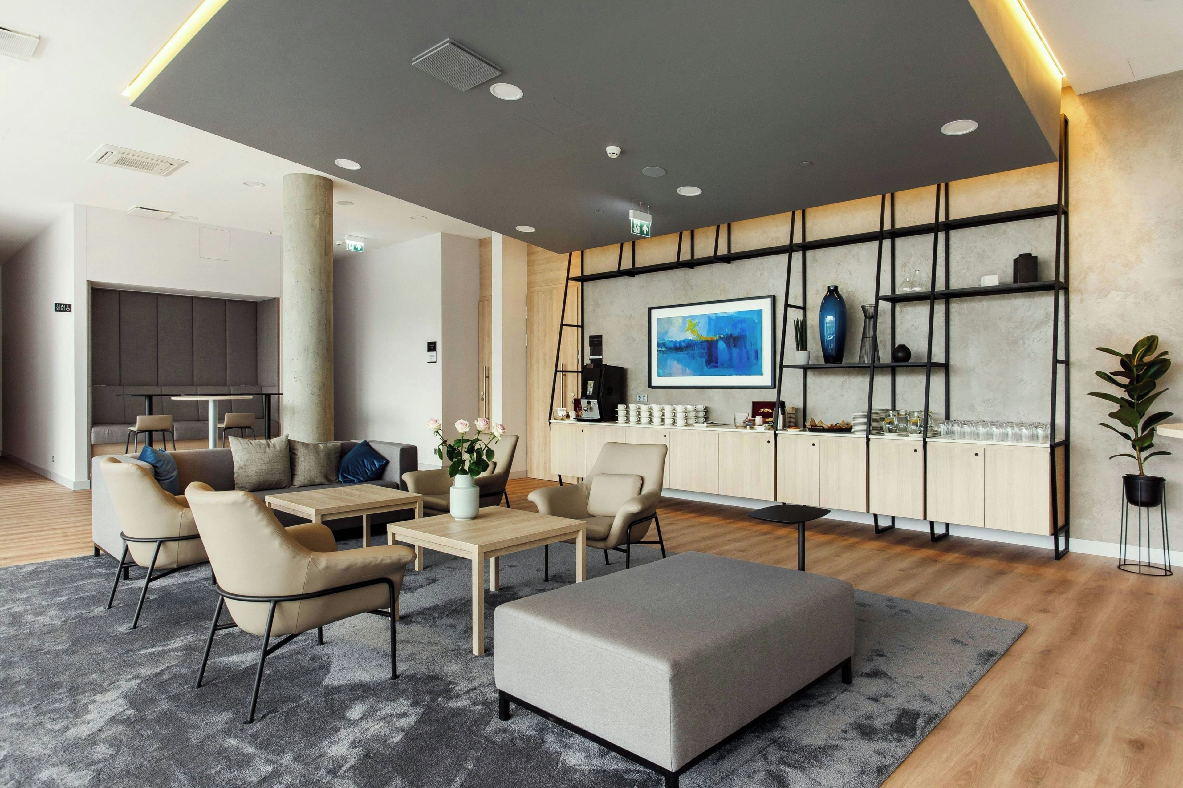 A modern hotel lobby with a seating area, a bar, and a kitchen in the background.