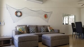 A modern living room with a sectional sofa, a dining area with a table and chairs, and a decorative wall hanging. - Tu Casa en Playa del Carmen conSportClub (Playa del Carmen)