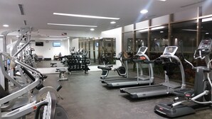 A modern gym with various cardio machines, weightlifting equipment, and a mirrored wall. - Tu Casa en Playa del Carmen conSportClub (Playa del Carmen)