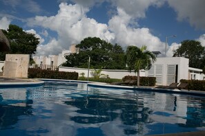 A swimming pool with clear blue water, surrounded by greenery and white buildings. - Tu Casa en Playa del Carmen conSportClub (Playa del Carmen)