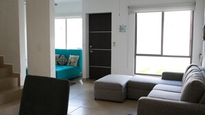 A living room with a sectional sofa, a teal couch, and a staircase leading to another level. - Tu Casa en Playa del Carmen conSportClub (Playa del Carmen)