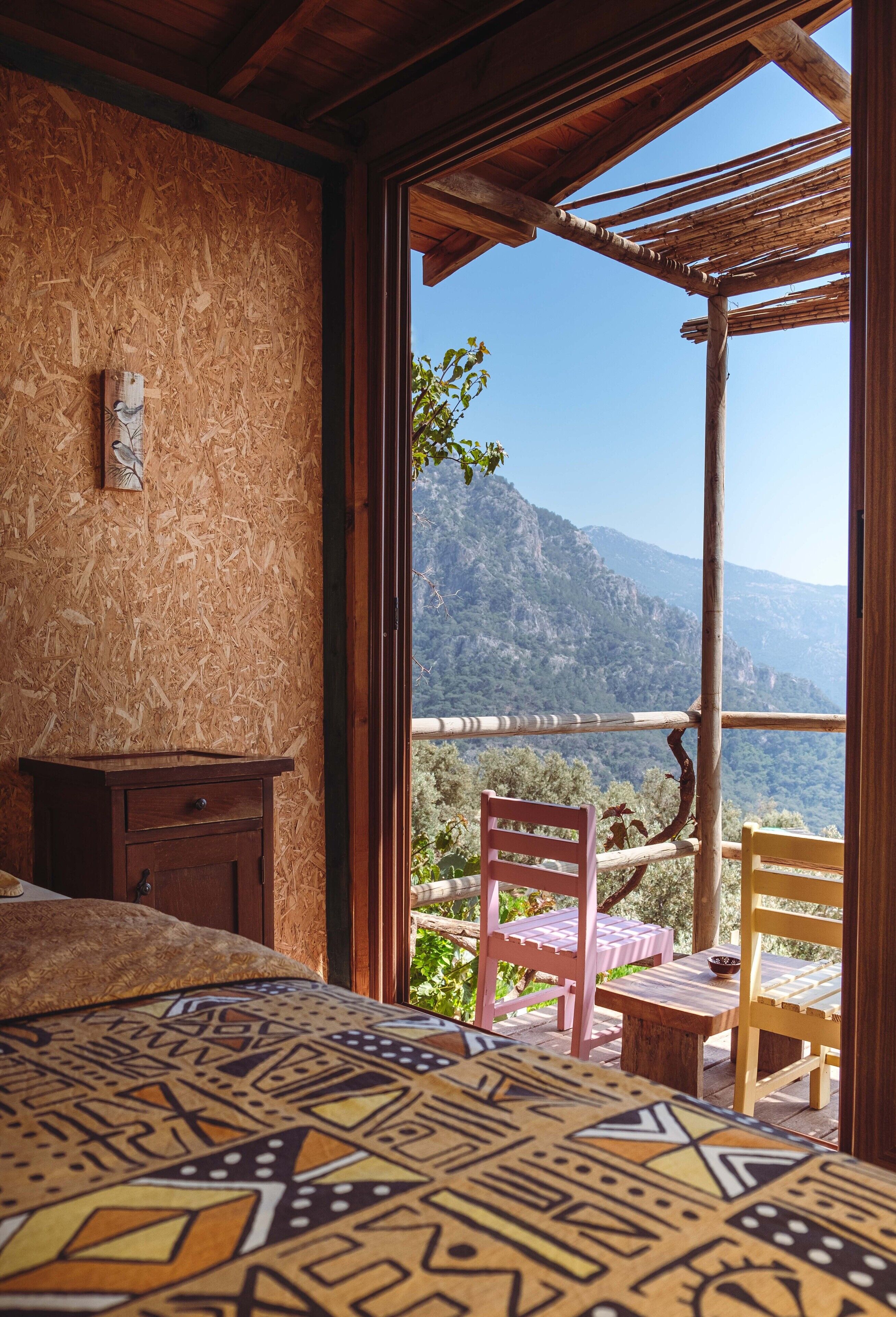 Une chambre à coucher avec un lit, une table de chevet en bois et une vue sur un balcon agrémenté de chaises et d’une table.