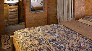 Un dormitorio de cabaña de madera con cama, espejo, lámpara colgante y cortina de macramé.