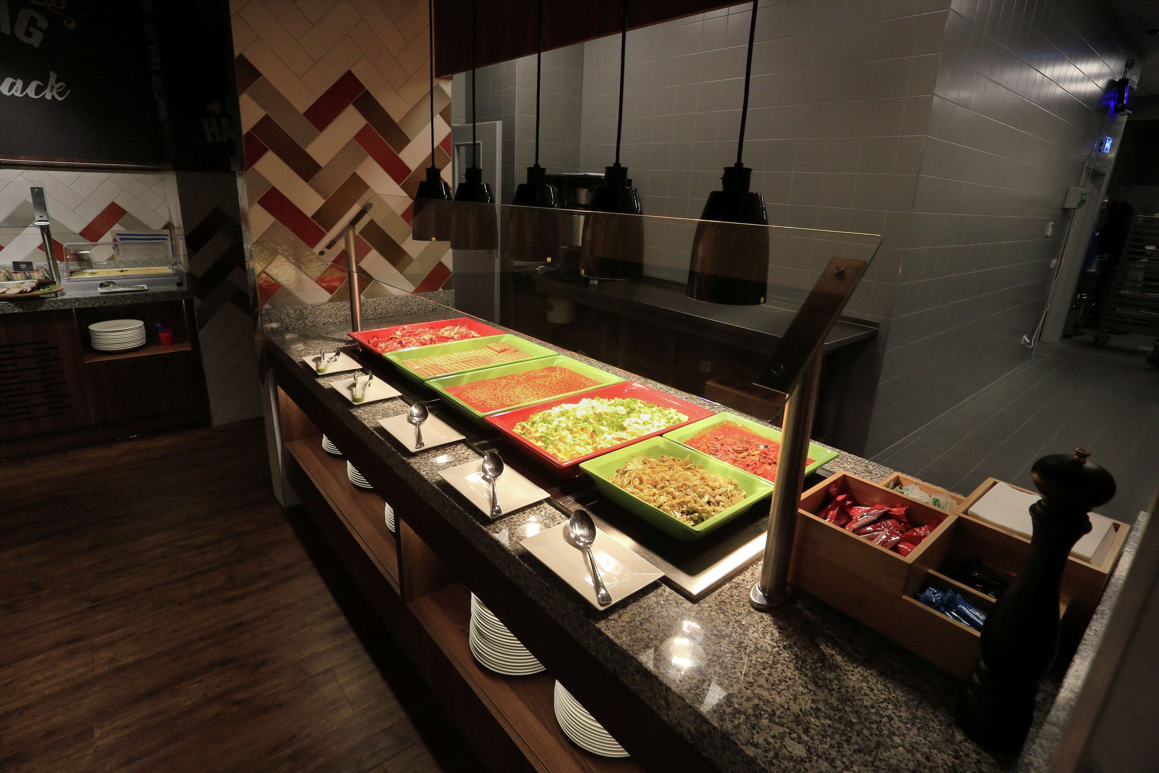 A buffet area with multiple food stations, a counter with plates and utensils, and a tiled wall with a chevron pattern.