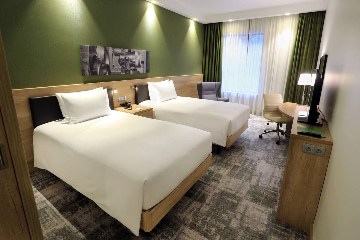 Ein Hotelzimmer mit zwei Betten, einem Schreibtisch, einem Stuhl und einem Fernseher.