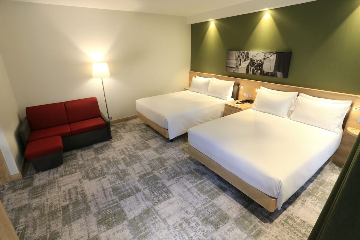 Ein Hotelzimmer mit zwei Betten, einem roten Sofa, einer Stehlampe und einem Bild an der Wand.