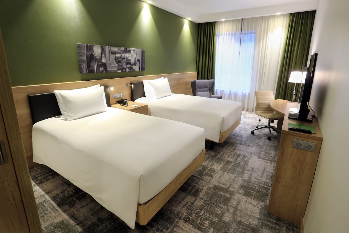Ein Hotelzimmer mit zwei Betten, einem Schreibtisch mit Stuhl, einem Fernseher und einer Lampe.