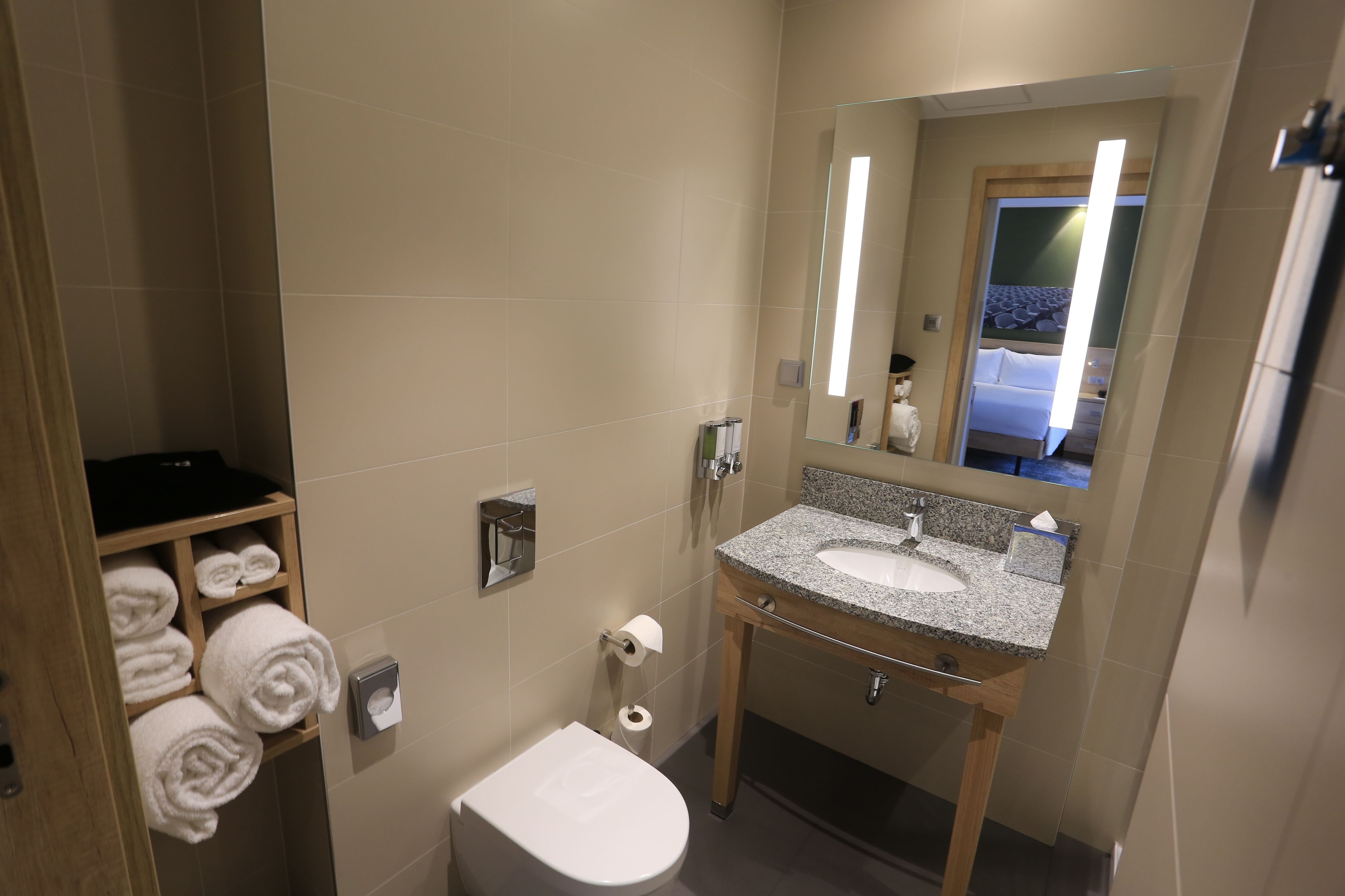 A modern bathroom with a granite sink, a toilet, and a towel rack with neatly folded towels.