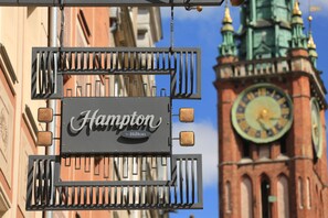 Ein Schild für Hampton by Hilton mit einem Glockenturm im Hintergrund.