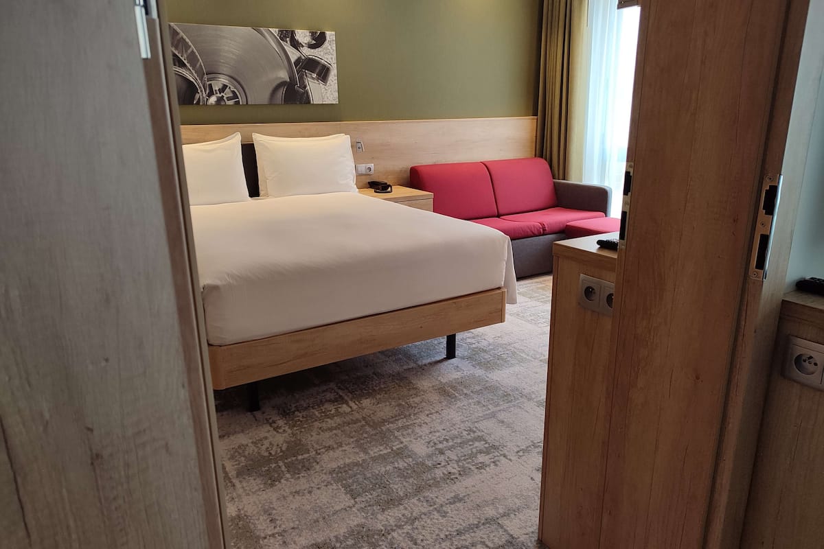 Ein Hotelzimmer mit einem Bett, einem roten Sofa, einem Nachttisch und einem an der Wand befestigten Kunstwerk.