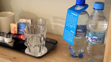 Een dienblad met een glas water, twee flessen Kropla Beskidu water, en een blauw informatief kaartje.