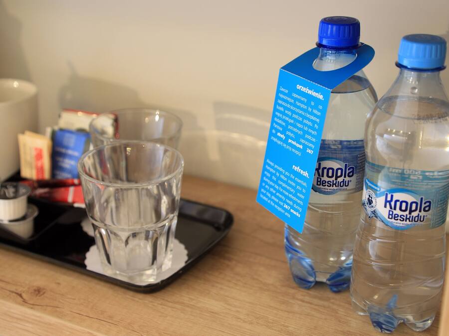 Een dienblad met een glas water, twee flessen Kropla Beskidu water, en een blauw informatief kaartje.