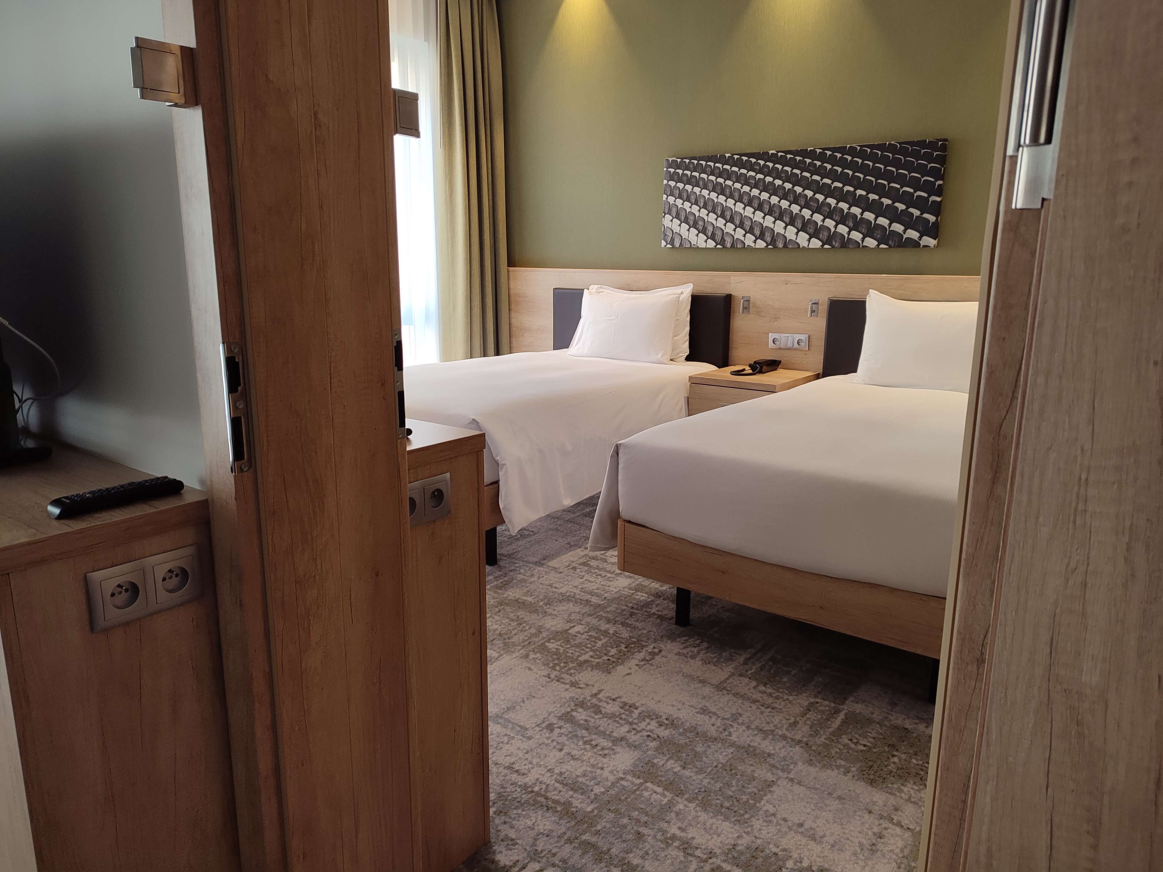 A hotel room with two beds, a wooden desk, a TV, and a wall-mounted artwork.