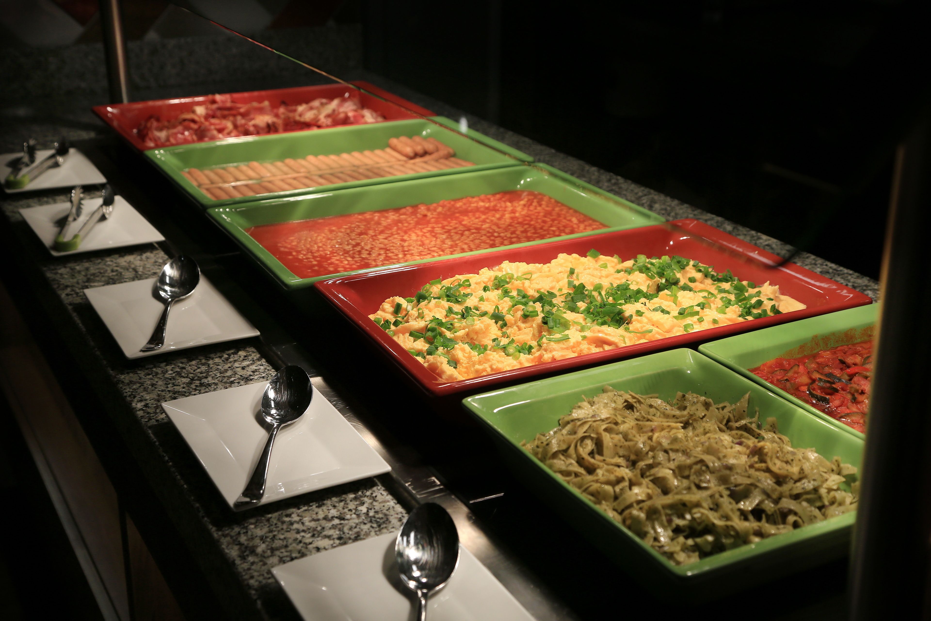 A buffet with various dishes in green and red trays.