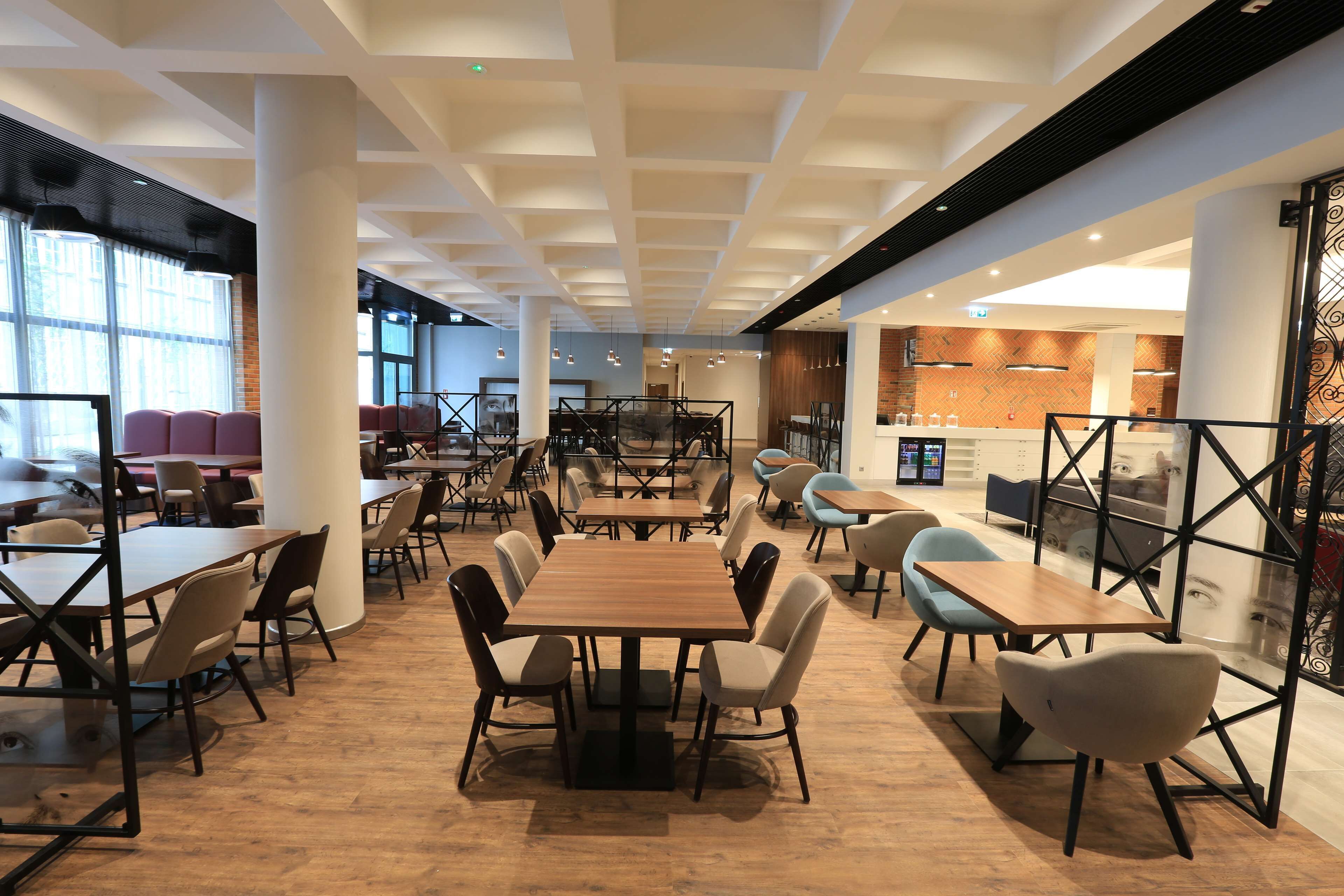 A spacious indoor area with multiple tables and chairs, large windows, and a modern ceiling design.