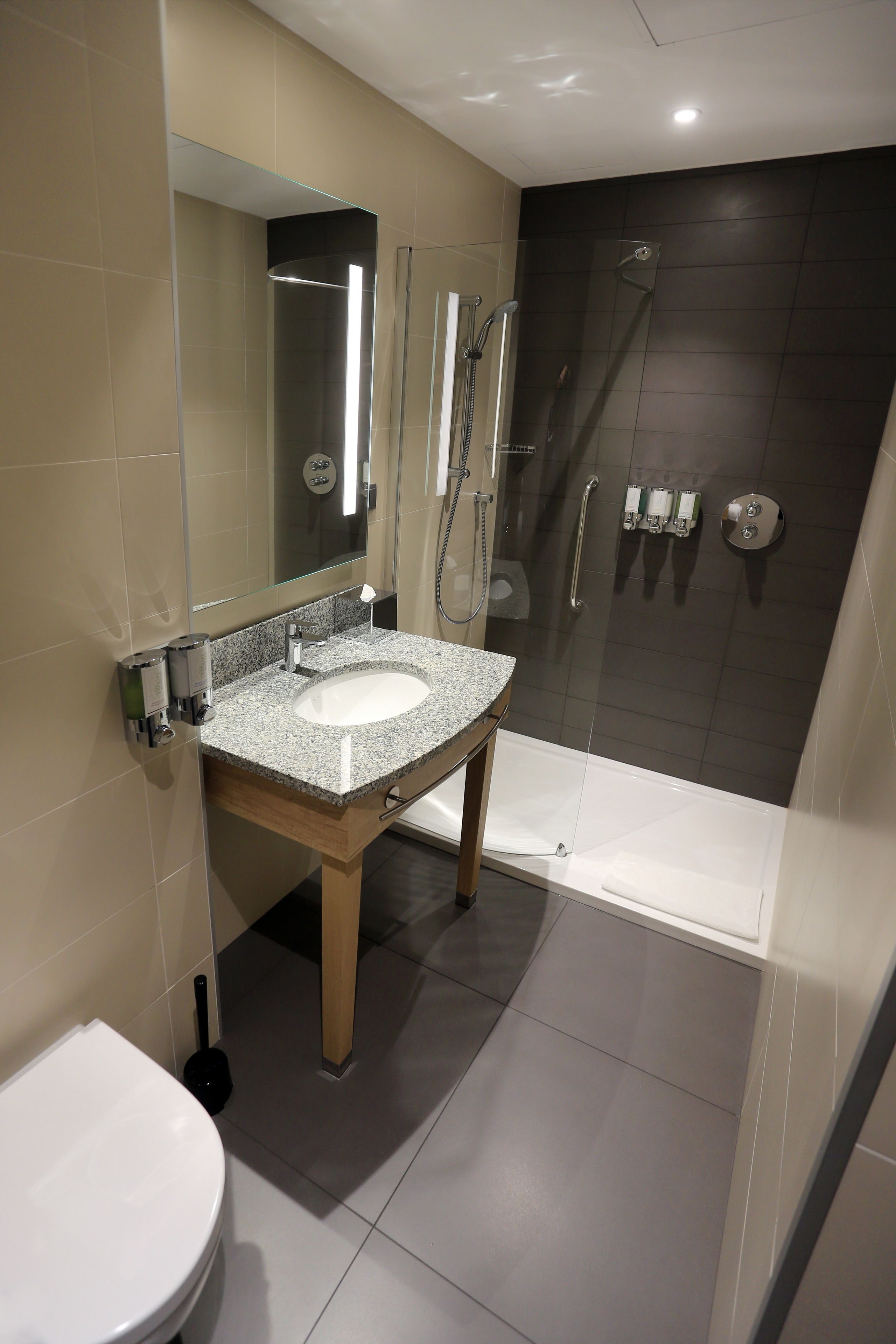 A modern bathroom with a granite sink, a toilet, a glass-enclosed shower, and a bathtub.