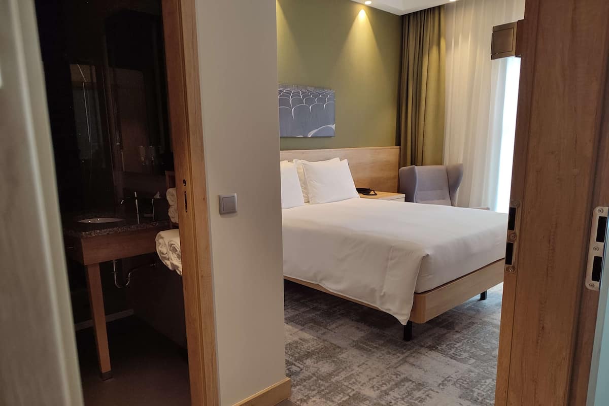 Ein Hotelzimmer mit Bett, Schreibtisch, Stuhl und einem durch eine offene Tür einsehbaren Badezimmer.