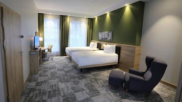 A hotel room with two beds, a desk with a computer, a chair, and a large window with curtains.