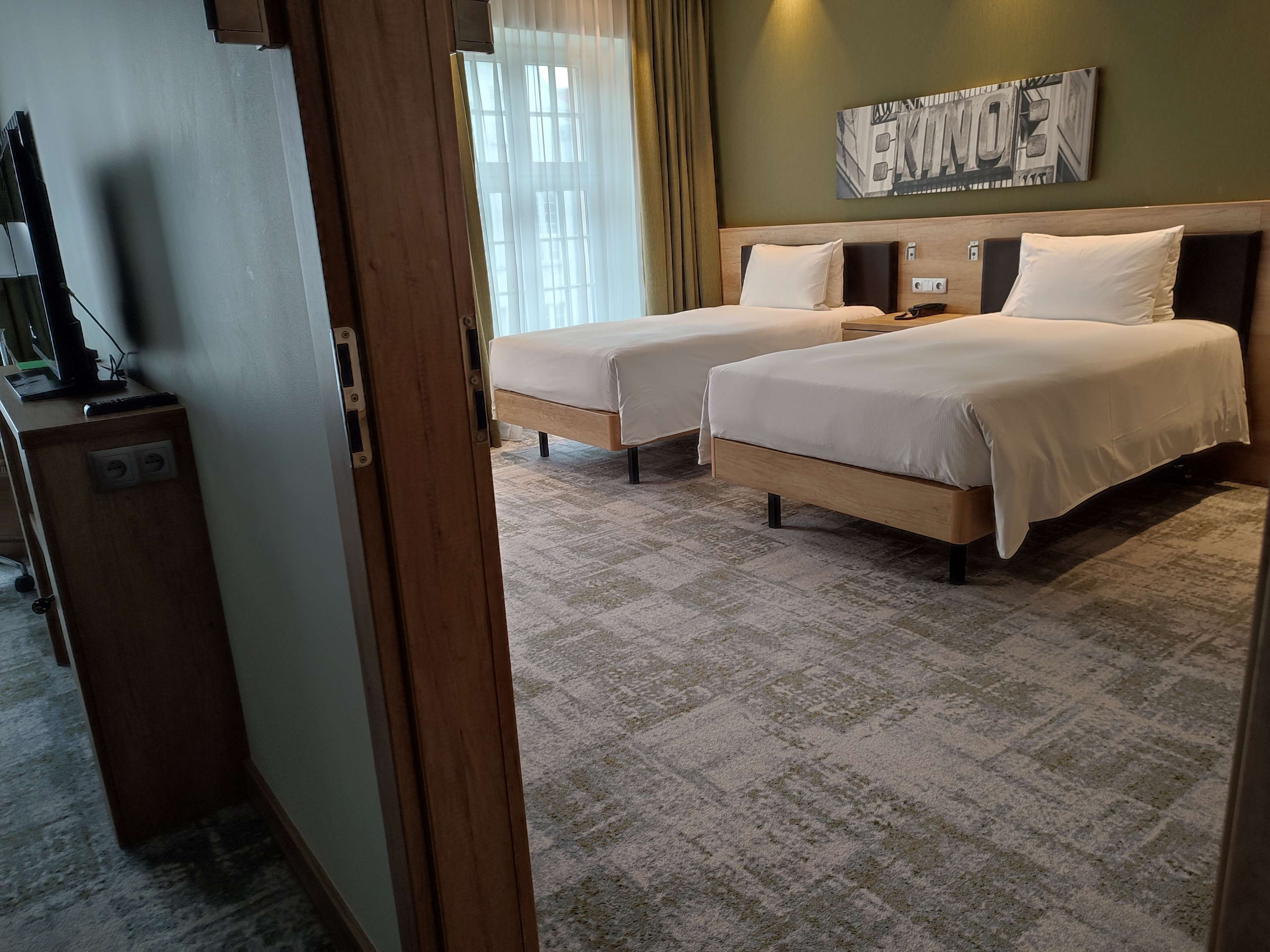 Habitación de hotel con dos camas, cabecero de madera, una obra de arte en la pared y suelo alfombrado.