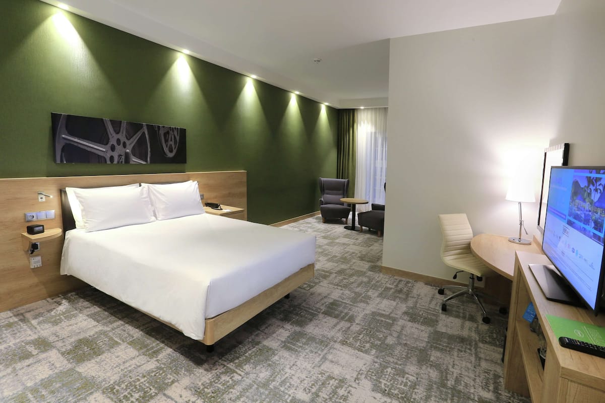 Ein Hotelzimmer mit einem Bett, einem Schreibtisch mit Computer, einem Sessel und einem Fernseher.