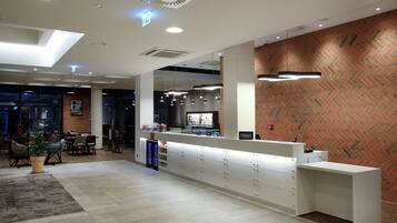 A hotel reception area with a modern design, including a reception desk, seating area, and a herringbone-patterned wall.