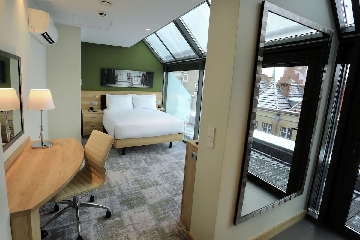 Ein Hotelzimmer mit Bett, Schreibtisch mit Stuhl, einem großen Fenster und Blick auf Gebäude.