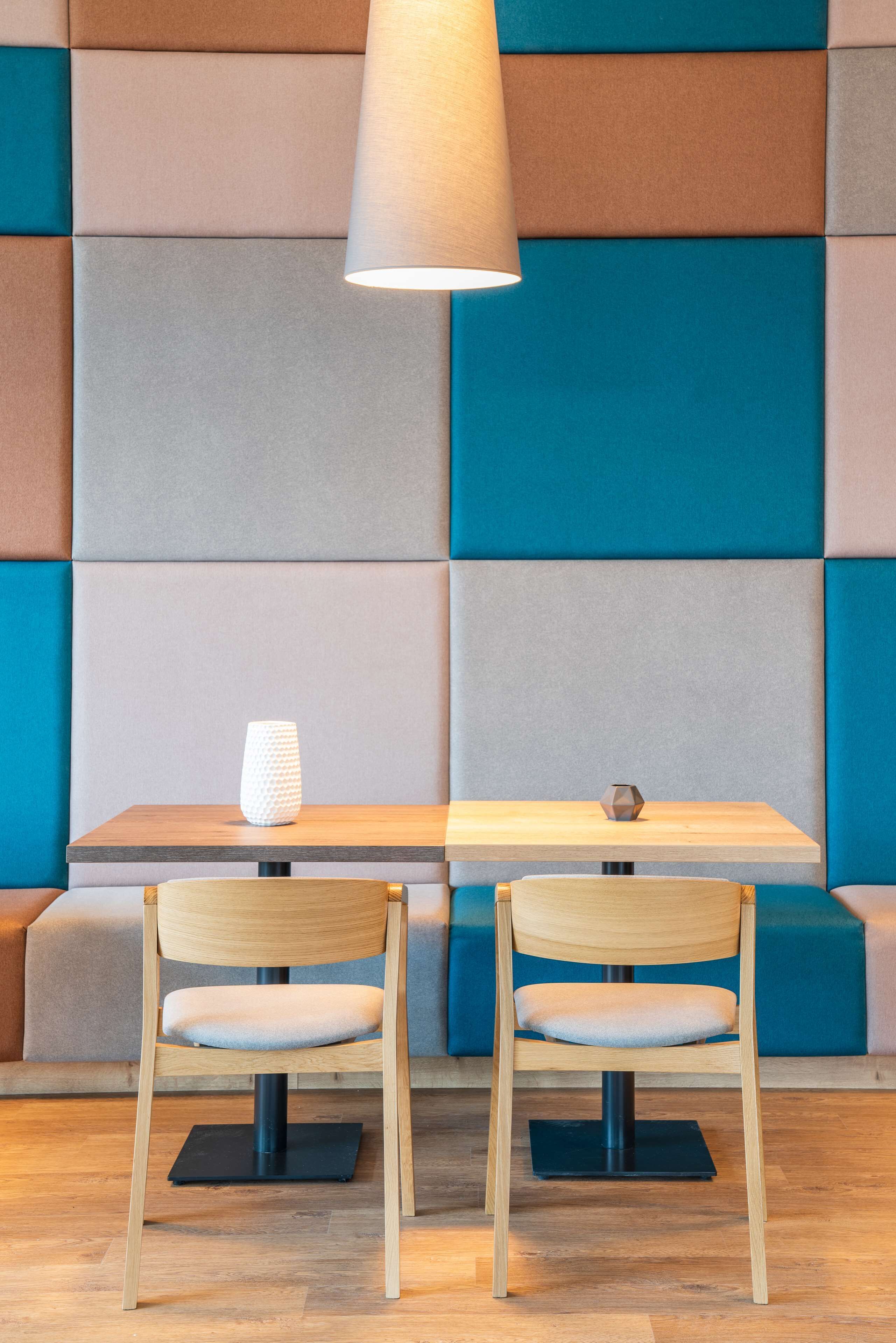 Un espace salon moderne avec une table et des chaises en bois, une lampe et un vase aux motifs géométriques.