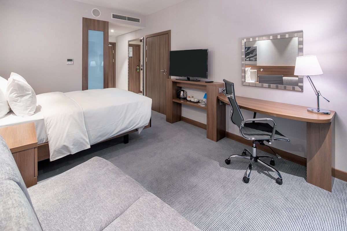 Ett hotellrum med en säng, ett skrivbord, en stol, en tv och en spegel.