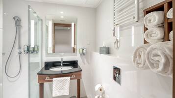 Un baño moderno con ducha envuelta en vidrio, tocador de madera con encimera negra y pared de azulejos blancos.