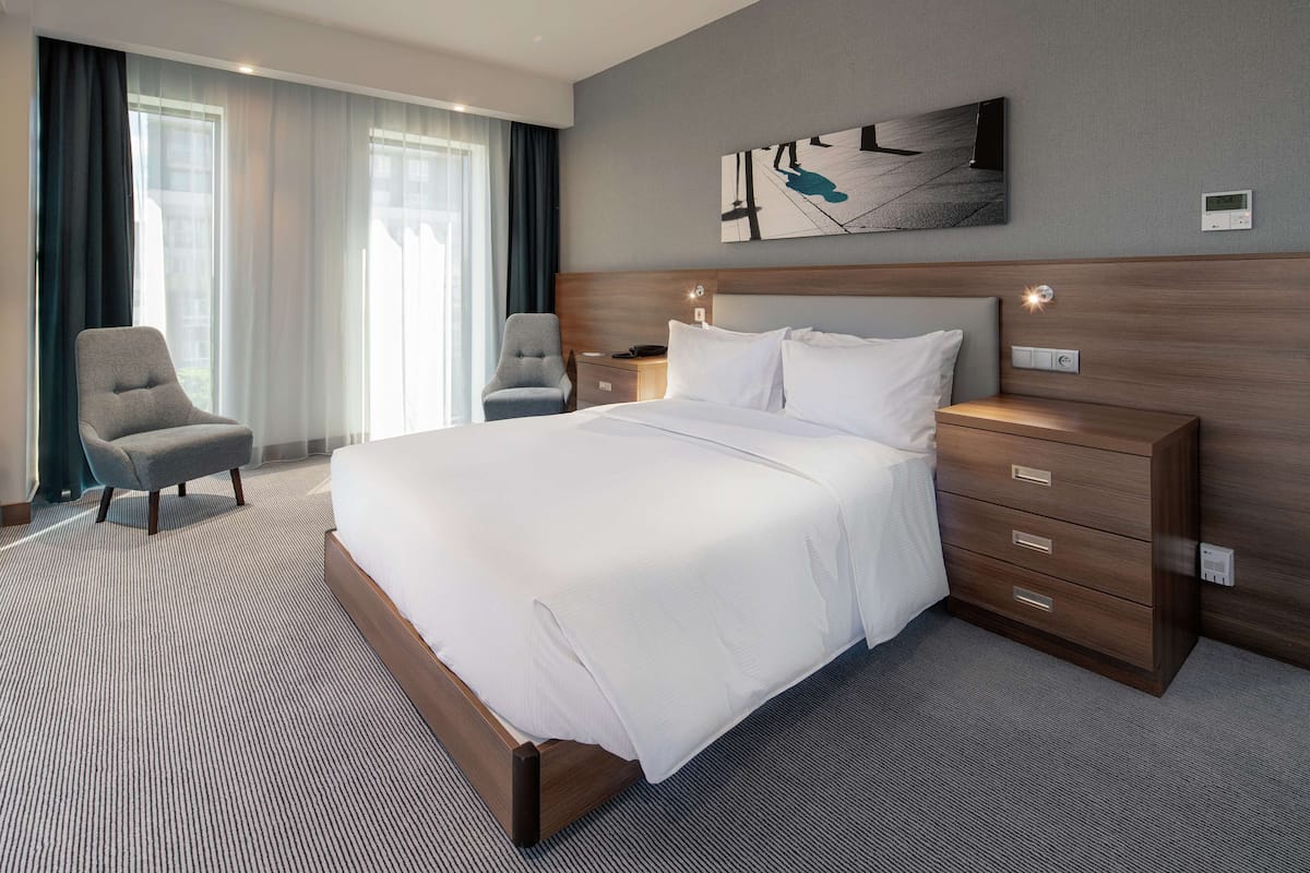 Ett hotellrum med en stor säng, två sängbord, en stol och ett konstverk som hänger på väggen.