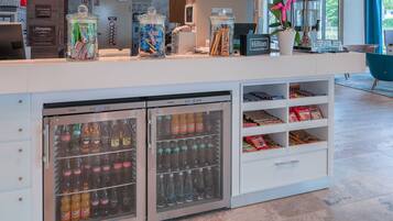 Een hotel receptie met een balie, twee drankdispensers en een plank met snacks.