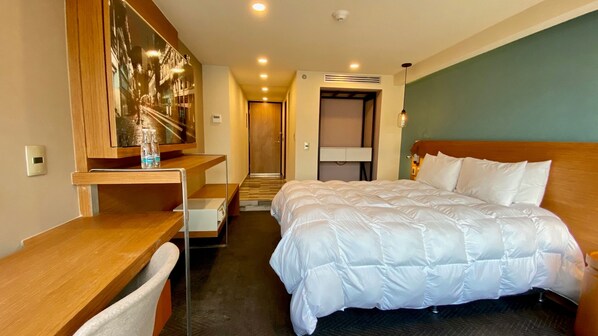 A hotel room with a large bed, a desk, a chair, a mirror, and a door leading to a hallway. - Hotel Cle Reforma Insurgentes (Mexico City)