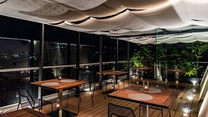 An outdoor dining area with tables and chairs, large windows, and potted plants. - Hotel Cle Reforma Insurgentes (Mexico City)