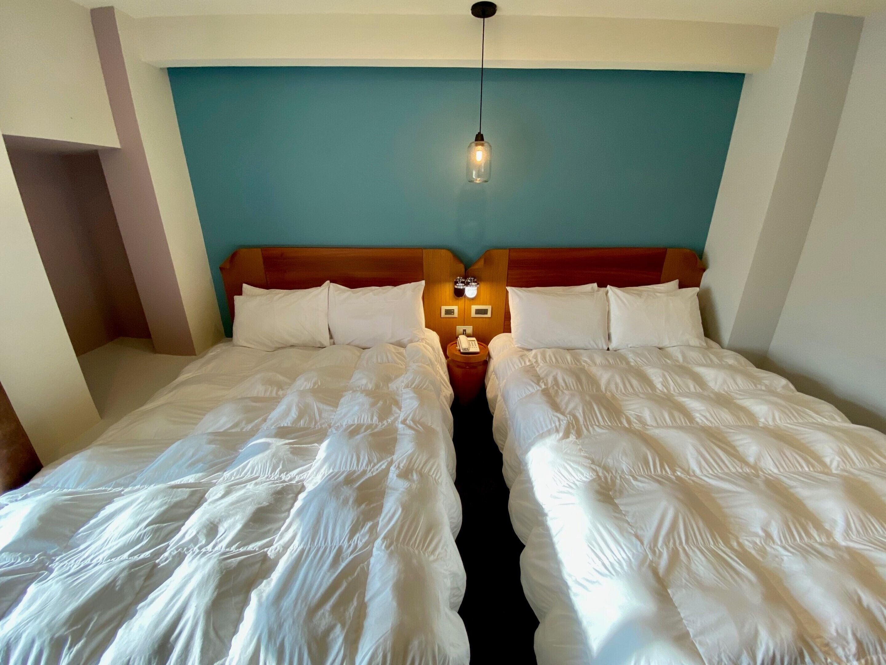 Una cama doble con ropa de cama blanca, cabecera de madera y mesita de noche con un teléfono.