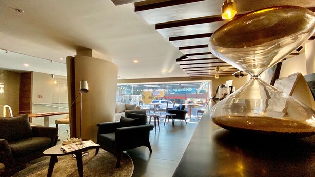 A modern interior with a large hourglass centerpiece, a glass partition, and a view of the street outside. - Hotel Cle Reforma Insurgentes (Mexico City)