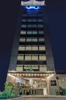 Un grand hôtel, reconnaissable à son enseigne « Cle » bien visible à l’entrée, avec une façade bien éclairée et un escalier menant au hall d’entrée.